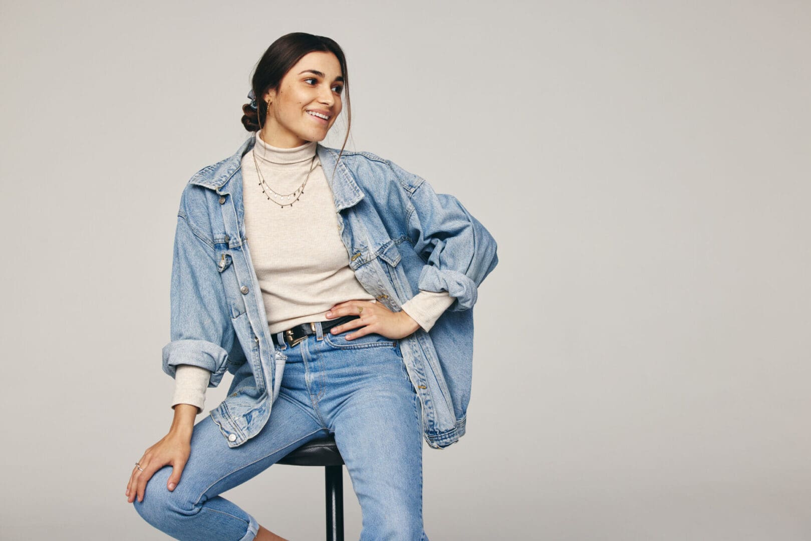 Woman in denim outfit sitting on stool.